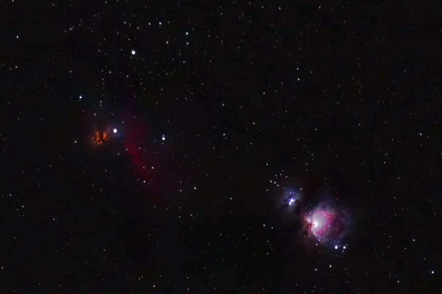 The Orion Nebula glowing pink and blue in a dense star field, with the orange Flame Nebula to its upper left